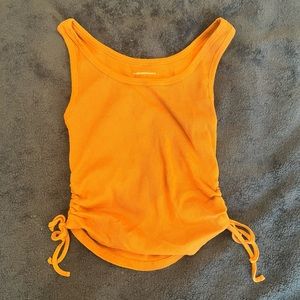 Muted orange colored ribbed tank top with strings on the sides to adjust crop.